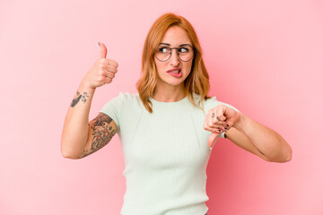 Young caucasian woman isolated on pink background showing thumbs up and thumbs down, difficult...