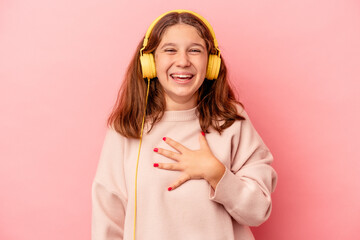 Little caucasian girl listening to music isolated on pink background laughs out loudly keeping hand...