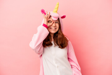 Obraz na płótnie Canvas Little caucasian girl wearing a unicorn pajama isolated on pink background excited keeping ok gesture on eye.