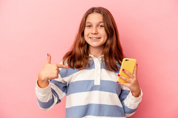 Little caucasian girl holding mobile phone isolated on pink background person pointing by hand to a shirt copy space, proud and confident