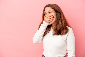 Little caucasian girl isolated on pink background thoughtful looking to a copy space covering mouth with hand.