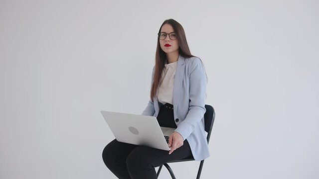 Strong confident business ledy in black glasses sitting with laptop on her lap on white isolated background and using touchpad