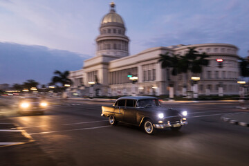 Fototapeta premium Old car on streets of Havana with Capitolio building in background. Cuba