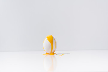 Yema de huevo líquida cayendo sobre un huevo blanco en una mesa blanca con fondo gris	