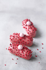 Pink Eclair with Raspberry Cream Filling, covered with pink chocolate and sprinkled with freeze-dried raspberries, on light grey background.