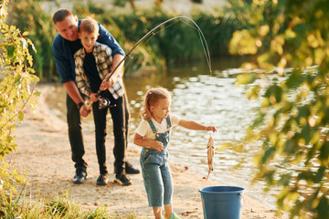 Girl putting fish into the bucket. Father with son and daughter on fishing together outdoors at...
