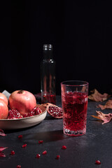 Jugo de granada con semillas y trozos de granada sobre fondo negro con hojas secas de otoño