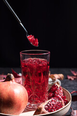 Jugo de granada con semillas y trozos de granada sobre fondo negro con hojas secas de otoño