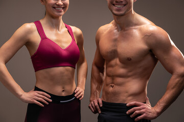 Fototapeta na wymiar Cropped view of the athletic man and woman posing to the camera before fitness exercise at the studio with brown wall