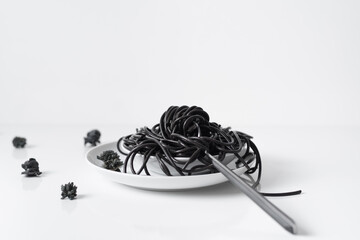 Espaguetis negros de sepia en un plato blanco con tenedor negro sobre fondo blanco