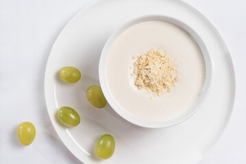 Crema de almendras, sopa fría española. Ajo blanco de Málaga con almendras y uvas en un recipiente blanco sobre una mesa blanca. Vista superior