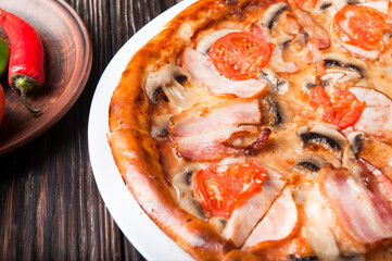 Meat pizza with pork slices and cheese lies on a white plate on a wooden table