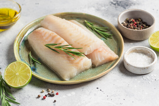 Fresh fish, raw cod fillets with rosemary, spices, lime and olive oil on kitchen table. Healthy seafood. closeup