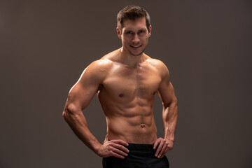 Fototapeta premium Horizontal view of the handsome muscular guy posing isolated on brown background, while showing his strong body and muscles
