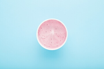 White paper cup of berry ice cream on light blue table background. Pastel color. Closeup. Cold sweet snack in summer. Top down view.