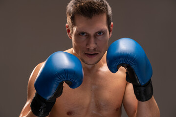 Angry fighter. Aggressive caucasian sports man in boxing gloves looking at the camera over brown background