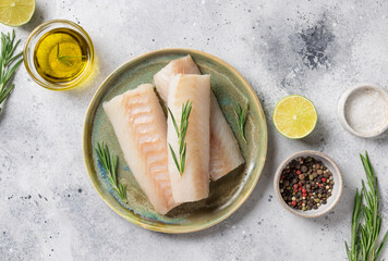 Raw cod fillet on ceramic plate with aromatic herbs, lime, salt and olive oil on gray background....