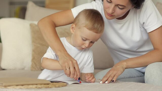 European family mom and son draw with pencils and read a book at home. single mother brings up a child, teaches him to draw, read and play, a beautiful woman and a cute boy have fun in their cozy home