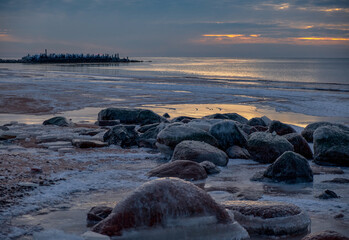 Ice blocks at the beach in winter evening by the sea with rocks