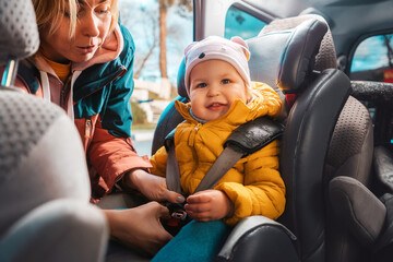 Portrait of smiling caucasian mother prepares her little adorable child for a trip by car. A woman...