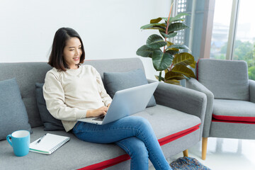 Obraz premium business woman Asian teenage girl sitting on the sofa drinking coffee and using a laptop inside the house. The concept is business, finance, working from home. online shopping internet
