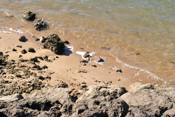 Fototapeta na wymiar Close Up of Sandy Beach with Rocks and Small Waves