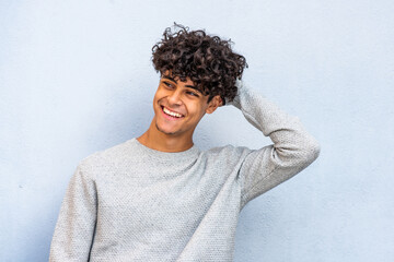young man laughing with hand in hair by blue wall