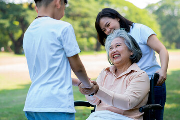 Happy senior Asian grandmother uses wheelchair with her daughter and grandchild in park, Grandson came to visit elderly grandmother and hold hand. Concept of happy family, good relationship together