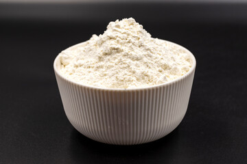 Bowl of flour on black background. Close-up. Horizontal view. Selective focus