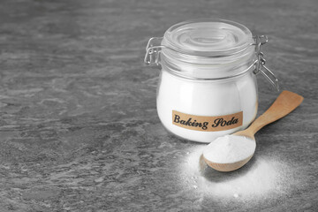 Wooden spoon and jar with baking soda on grey table. Space for text