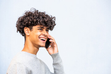 Close up side of happy young North African man laughing while talking with cellphone by gray...