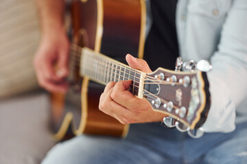 Close up view. Man in casual clothes and with acoustic guitar is indoors