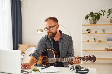 Writing some ideas. Man in casual clothes and with acoustic guitar is indoors