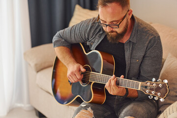 Man in casual clothes and with acoustic guitar is indoors