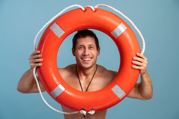 Waist up portrait view of nice attractive cheerful confident guy rescuer carrying rubber lifesaver and looking through it isolated over bright vivid vibrant blue color background