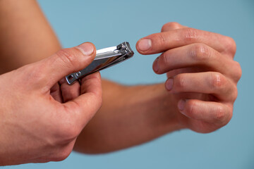 Hand manicure with nail clipper concept. Close up view of the man cutting his nails over the blue background. Stock photo