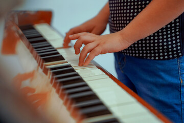 Hands of a boy playing the piano. Selective focus, to kid fingers and piano key to play the piano. Back to school concept. Online course piano. Blurred background.