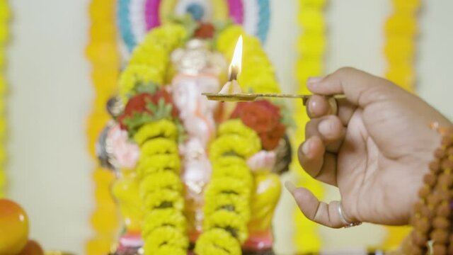 close up shot of hand offering mangalaarthi to lord ganesh idol during festival celebration at home - concept of treditional festival and rituals.