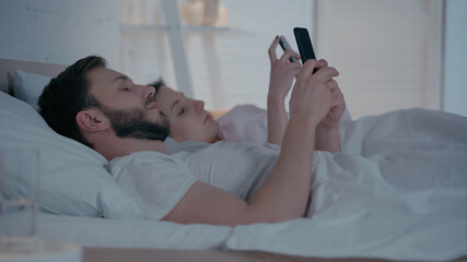 Obraz na płótnie Canvas Young couple using smartphones on bed at home.