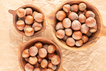 Several unpeeled hazelnuts in three wooden cups on craft paper, close-up, top view.