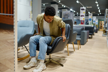 Young man choosing chair in furniture store