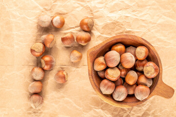 Several unpeeled hazelnuts in a wooden cup on craft paper, close-up, top view.