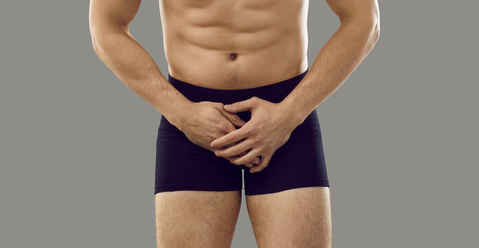 Man in underwear standing isolated on grey background covering his painful crotch area. Cropped shot, banner. Male intimate health problems, sexually transmitted diseases, testicular cancer concept