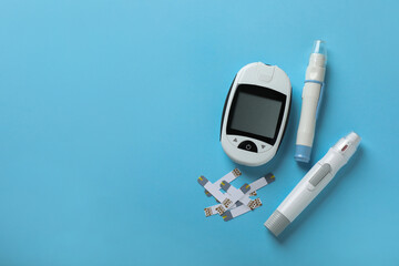 Digital glucometer, lancet pens and test strips on light blue background, flat lay with space for...