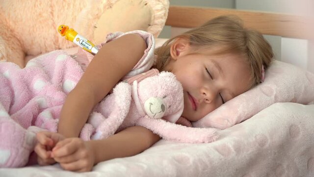 Sick little child in bed with thermometer coughs in sleep. Fathers hands check temparaura with thermometer. Treatment in illness.