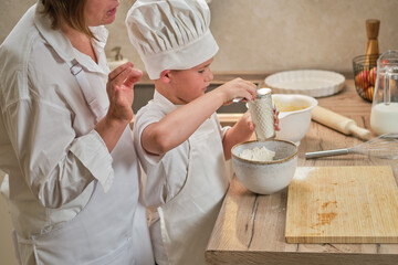 Mother and son cooking apple pie in the home kitchen. A woman and a boy in chef hats and aprons...