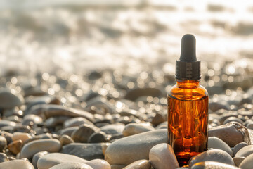 Brown glass cosmetic bottle with black pipette on stone pebble beach on sunny day. Natural beauty concept.