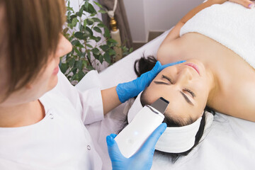 Obraz na płótnie Canvas Specialist cosmetologist making facial procedure treatment to a patient woman using ultrasonic skin equipment.