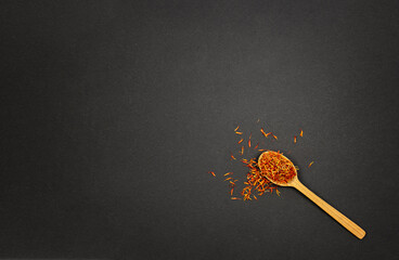 Fototapeta na wymiar Red saffron spice in wooden spoon on black background with copy paste