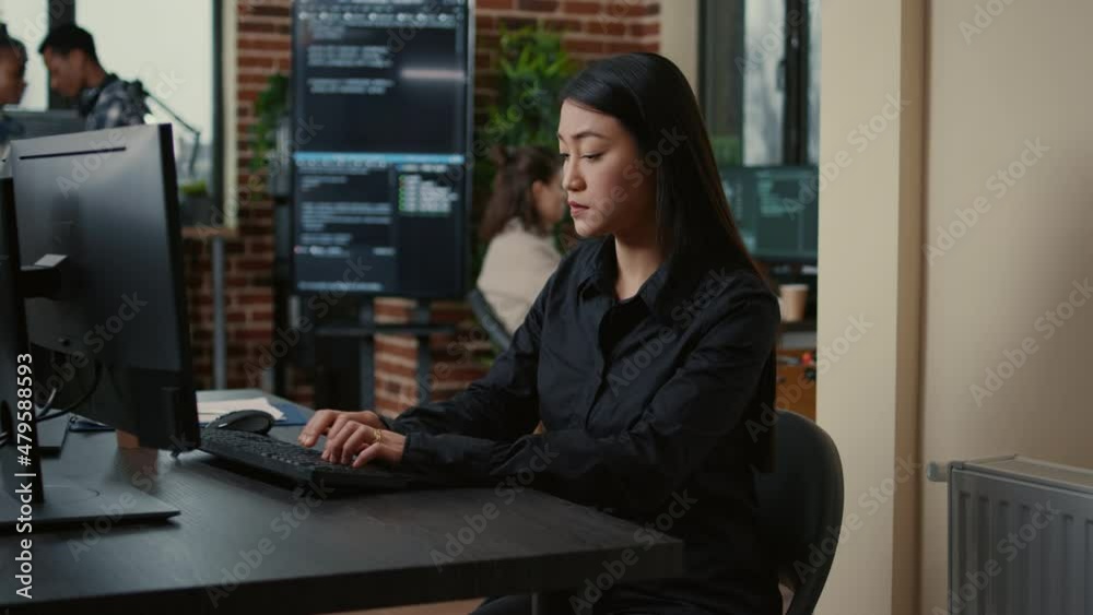 Poster system engineer focused on writing code sitting at desk in software development office while team of
